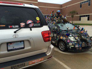 A car with many stickers on it's hood and other cars parked in front of it.