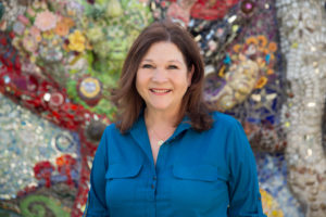 A woman standing in front of a wall covered with colorful artwork.