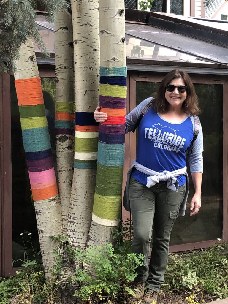 A woman standing next to a tree with yarn wrapped around it.