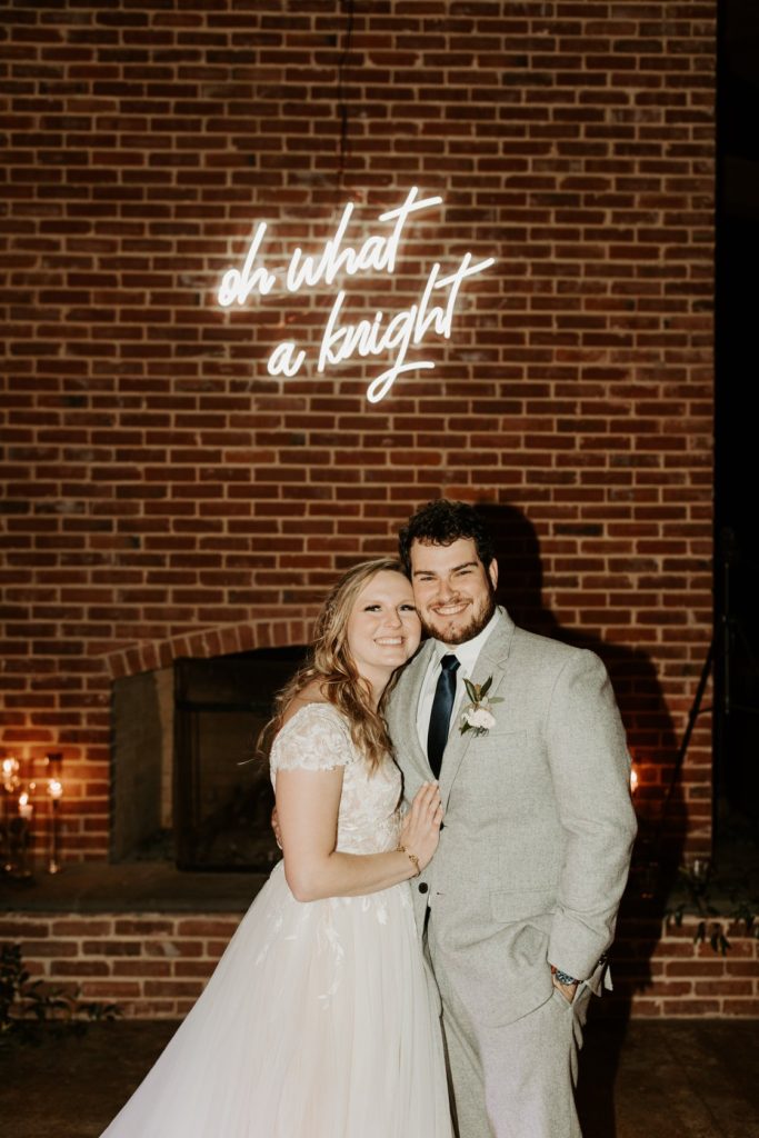 A couple poses for a picture in front of a brick wall.