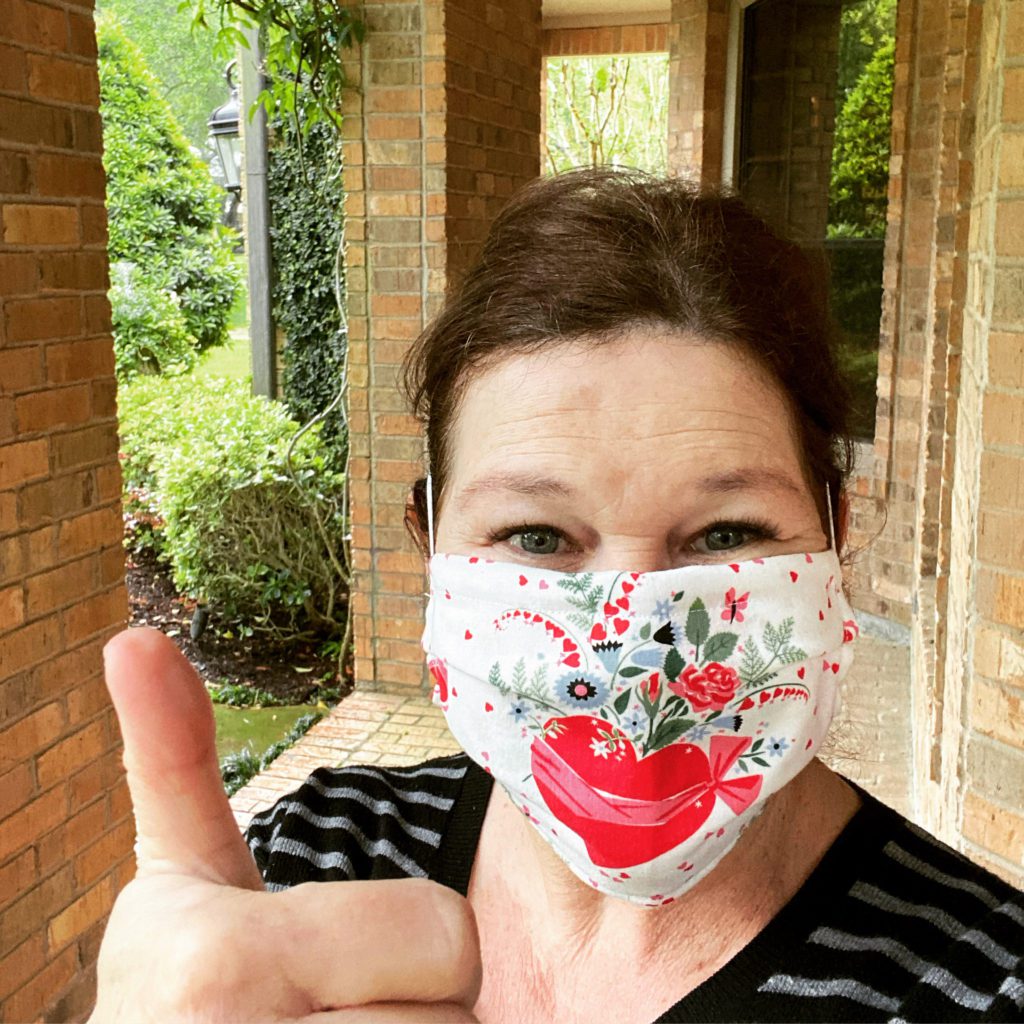 A woman wearing a face mask giving the peace sign.