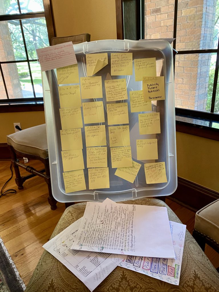 A plastic container with many yellow post it notes on top of papers.